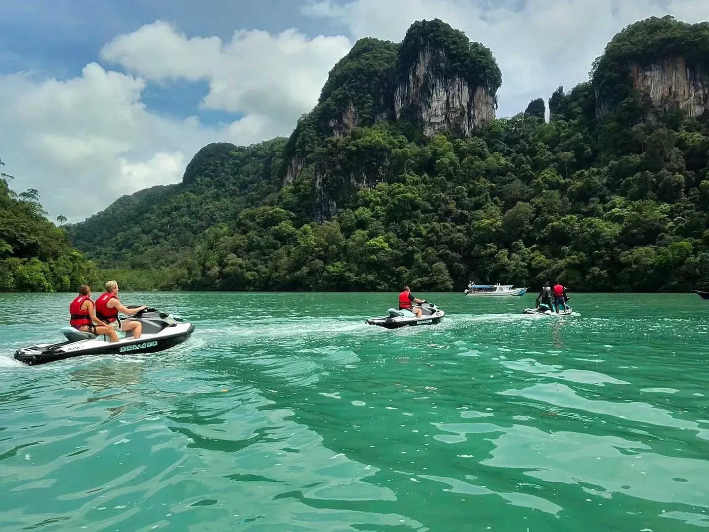 Jet skis on turquoise water below limestone hills, Langkawi